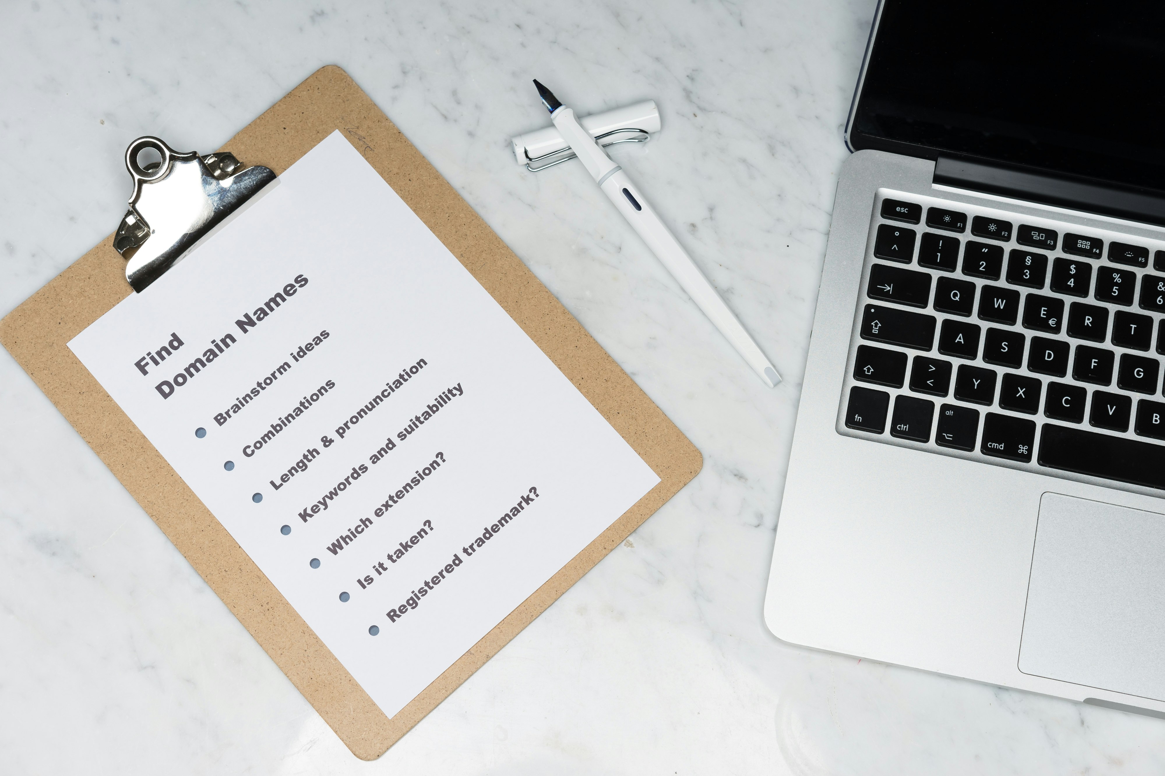 Clipboard with "Find Domain Names" list and laptop with pen